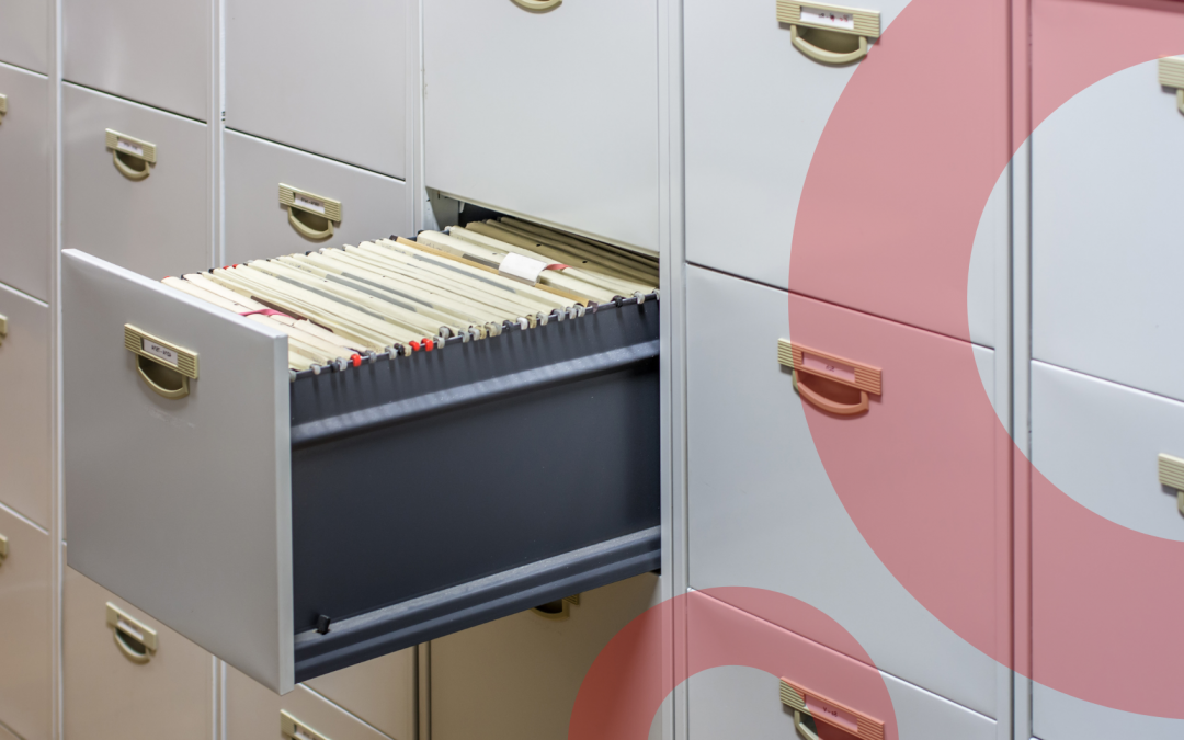 Grey metal filing cabinet with one open drawer containing paper card files